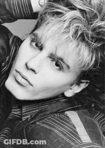 A Black And White Photo Of A Young Man With Curly Hair And A Striped Shirt . GIF