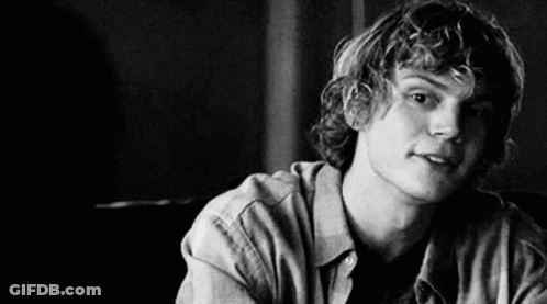 A Black And White Photo Of A Young Man With Curly Hair Sitting At A Table . GIF
