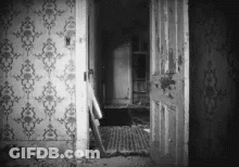 A Black And White Photo Of An Old House With A Door Open And A Staircase . GIF
