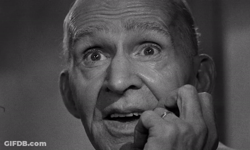 A Black And White Photo Of An Older Man With His Hand On His Mouth GIF