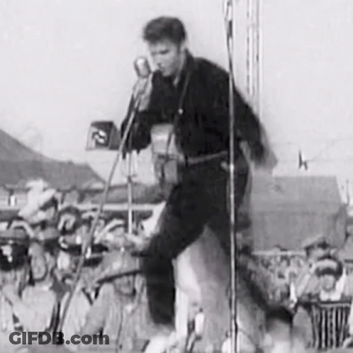 A Black And White Photo Of Elvis Presley Playing A Guitar And Singing Into A Microphone On A Stage . GIF