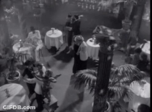A Black And White Photo Of People Dancing In A Room With Tables GIF