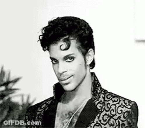 A Black And White Photo Of Prince In A Suit And Necklace . GIF