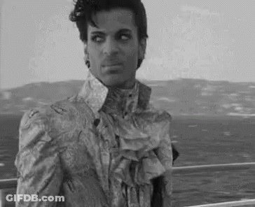 A Black And White Photo Of Prince Wearing A Ruffled Shirt And Tie . GIF