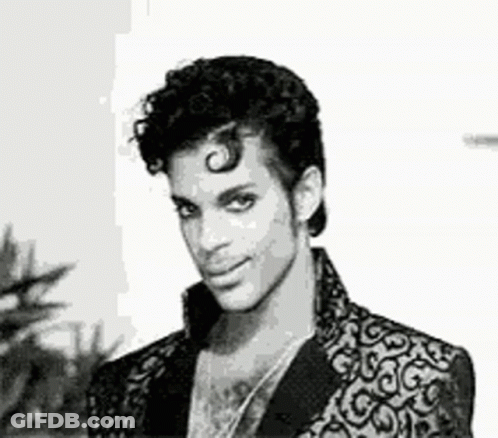 A Black And White Photo Of Prince Wearing A Suit Jacket And Necklace . GIF