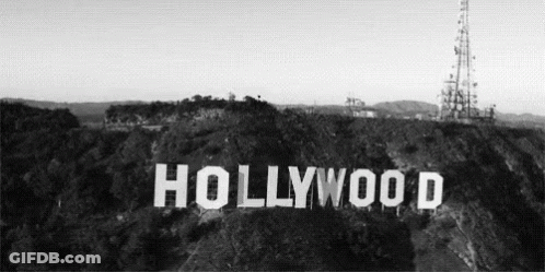 A Black And White Photo Of The Hollywood Sign Sitting On Top Of A Hill Surrounded By Trees . GIF