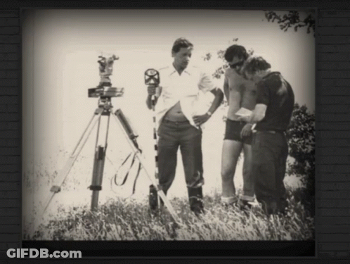 A Black And White Photo Of Three Men Standing In A Field With A Camera On A Tripod GIF