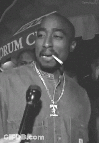 A Black And White Photo Of Tupac Shakur Smoking A Cigarette While Holding A Microphone . GIF