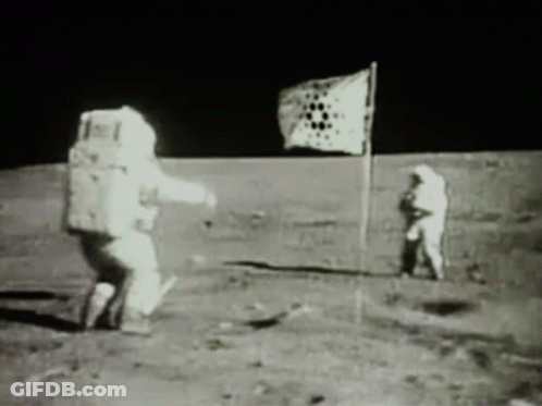 A Black And White Photo Of Two Astronauts On The Moon With A Flag In The Background GIF