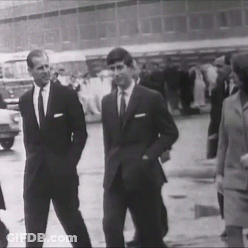 A Black And White Photo Of Two Men In Suits Standing Next To Each Other On A Street . GIF