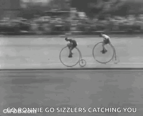 A Black And White Photo Of Two Men Riding Bicycles On A Road . GIF