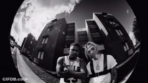 A Black And White Photo Of Two Men Standing In Front Of A Building With One Wearing A Number 25 Jersey GIF