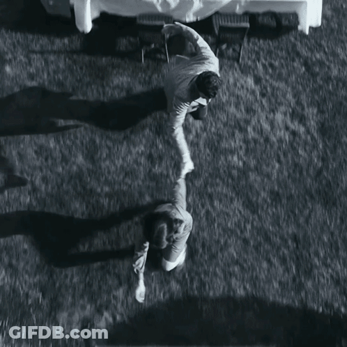 A Black And White Photo Of Two People Standing Next To Each Other On A Grassy Field GIF