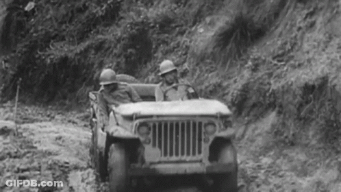 A Black And White Photo Of Two Soldiers Driving A Jeep Down A Dirt Road . GIF