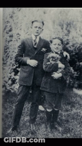 A Black And White Photo Of Two Young Boys Holding A Dog GIF