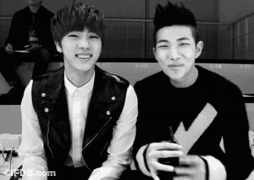 A Black And White Photo Of Two Young Men Sitting Next To Each Other And Smiling . GIF