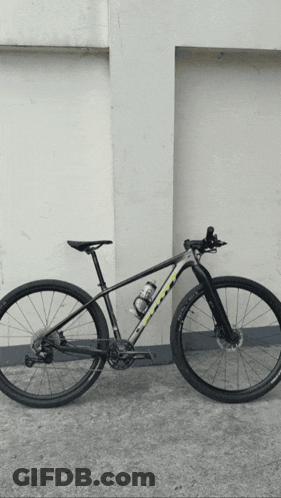A Black And Yellow Bicycle Is Parked In Front Of A Wall GIF