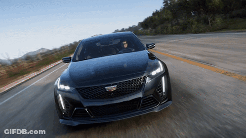 A Black Cadillac Is Driving Down A Road With Mountains In The Background GIF
