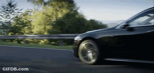 A Black Car Is Driving Down A Country Road GIF