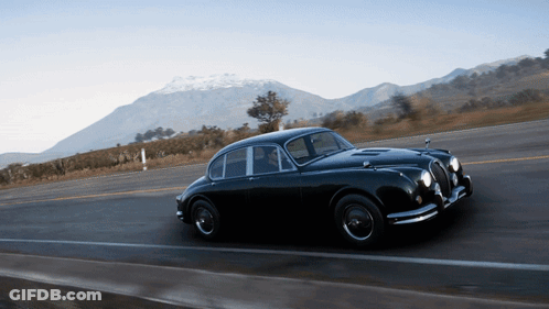 A Black Car Is Driving Down A Road In Front Of Mountains GIF