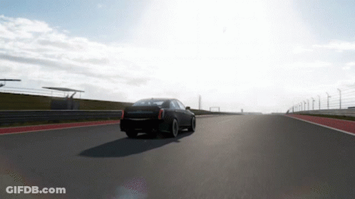 A Black Car Is Driving Down A Road With A Fence In The Background GIF