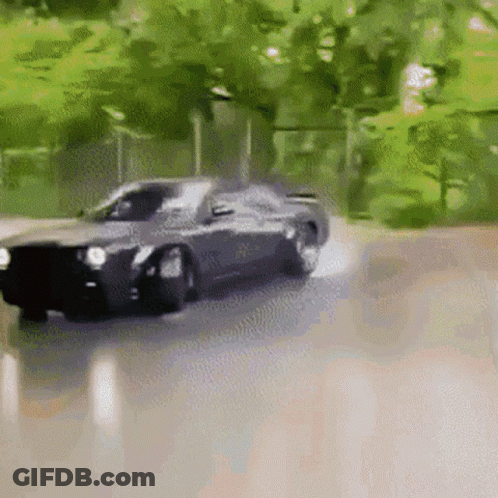 A Black Car Is Driving Down A Road With Trees In The Background And Smoke Coming Out Of The Tires . GIF