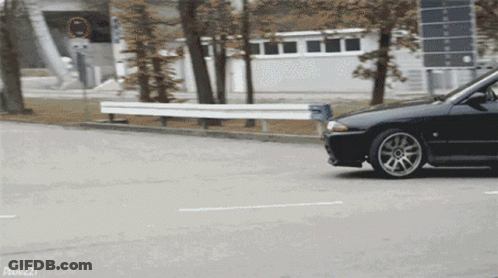 A Black Car Is Driving Down A Street With A Sign That Says No Trucks GIF