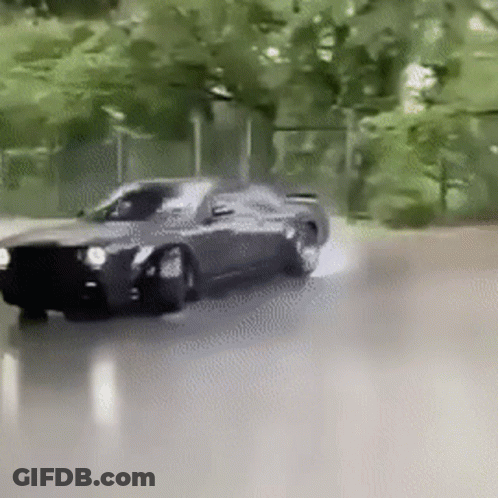 A Black Car Is Driving Down A Street With Trees In The Background . GIF