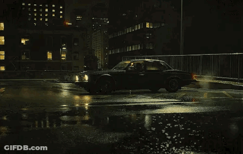 A Black Car Is Driving On A Wet Street At Night . GIF