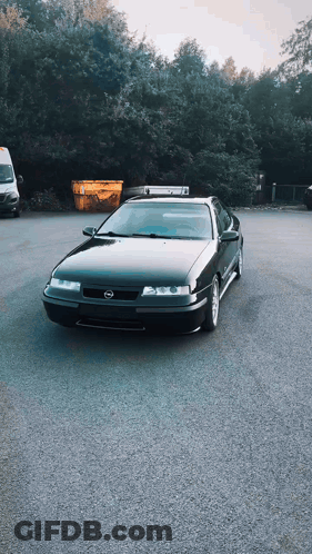 A Black Car Is Parked In A Parking Lot Next To A Yellow Dumpster GIF