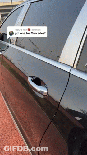 A Black Car Is Parked On The Side Of The Road Next To A Post That Says " Got One For Mercedes " GIF