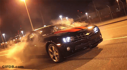 A Black Car With An Orange Stripe On The Side Is Driving Down A Street At Night GIF
