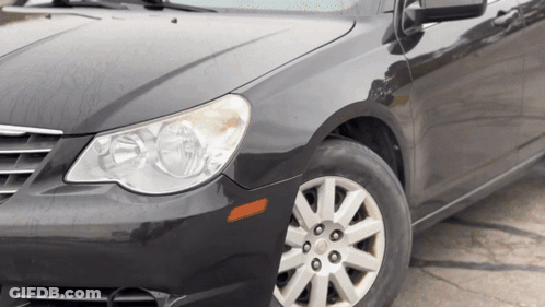 A Black Car With Silver Rims And A Black Hood Is Parked On The Side Of The Road GIF