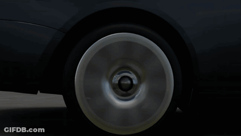 A Black Car With White Wheels Is Parked On A Street GIF