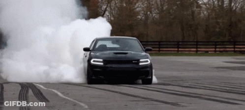A Black Dodge Charger Is Doing A Burnout On A Road GIF