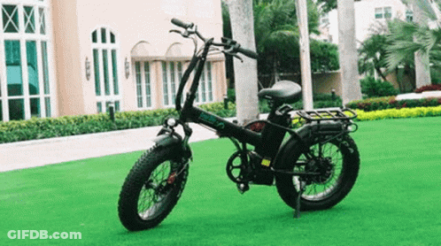 A Black Folding Electric Bike Is Parked On A Lush Green Field . GIF