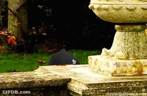 A Black Hat With A Heart On It Is Sitting On A Stone Ledge Next To A Statue .. GIF