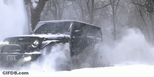 A Black Jeep Is Driving Through A Snowy Forest . GIF