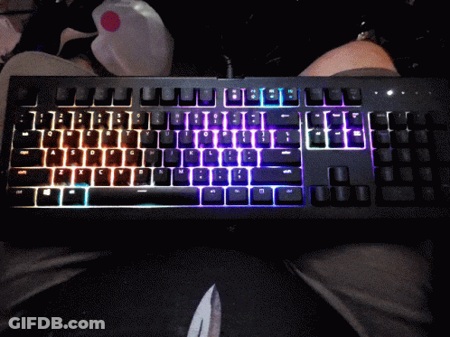 A Black Keyboard With Rainbow Colored Keys Is Sitting On A Persons Lap GIF