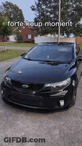 A Black Kia Car Is Parked In A Driveway With The Words Forte Koup Moment Above It GIF