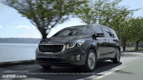 A Black Kia Minivan Is Driving Down A Street Near A Body Of Water GIF