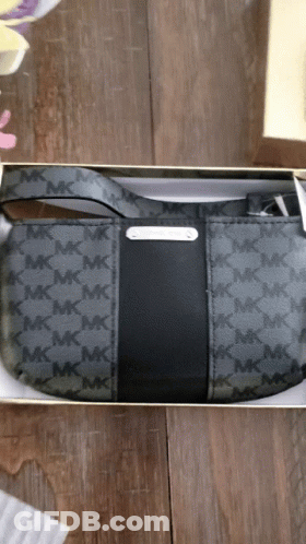 A Black Michael Kors Purse Is In A Box On A Wooden Table GIF