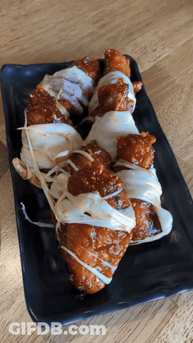 A Black Plate Topped With Fried Chicken Covered In Sauce And Cheese GIF