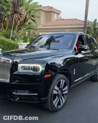 A Black Rolls Royce Is Parked In Front Of A House With Palm Trees GIF