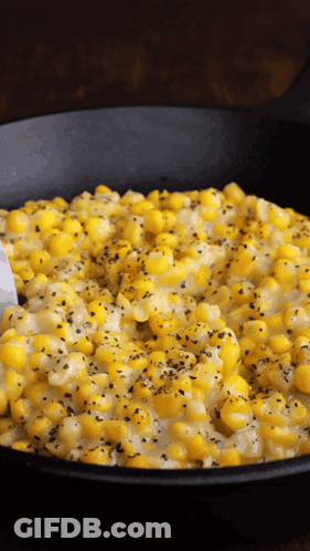 A Black Skillet Filled With Corn And Cheese With A Spoon In It GIF