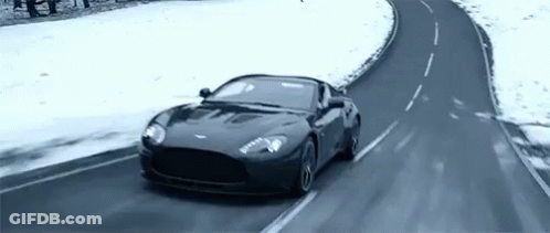 A Black Sports Car Is Driving On A Snowy Road . GIF