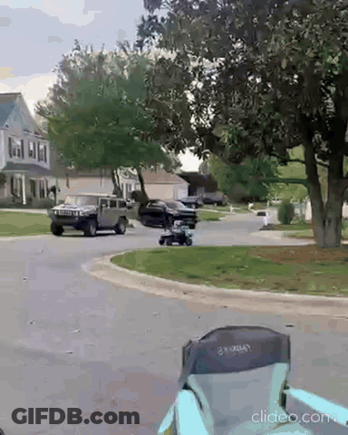 A Black Suv Is Driving Down A Residential Street Next To A Lawn Mower GIF