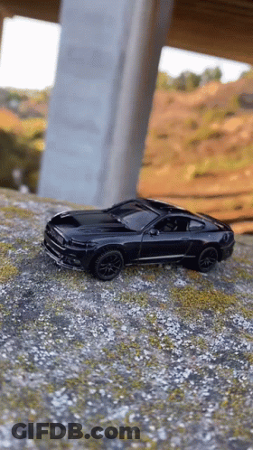 A Black Toy Car Is Sitting On Top Of A Dirt Hill Under A Bridge . GIF