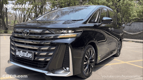 A Black Toyota Minivan Is Parked In A Parking Lot With Trees In The Background GIF