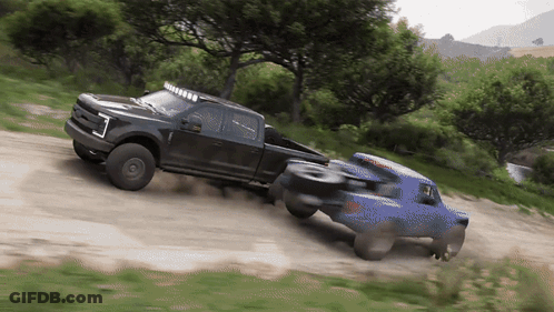 A Black Truck Pulls A Blue Truck On A Dirt Road GIF